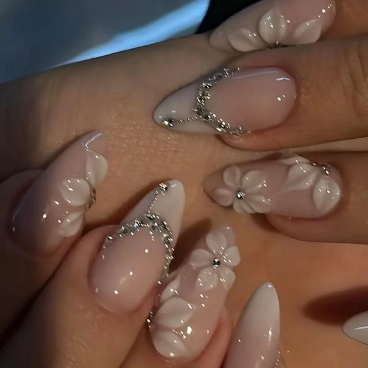 Long almond nails with pale pink bases, white 3D flowers and silver rhinestone curves