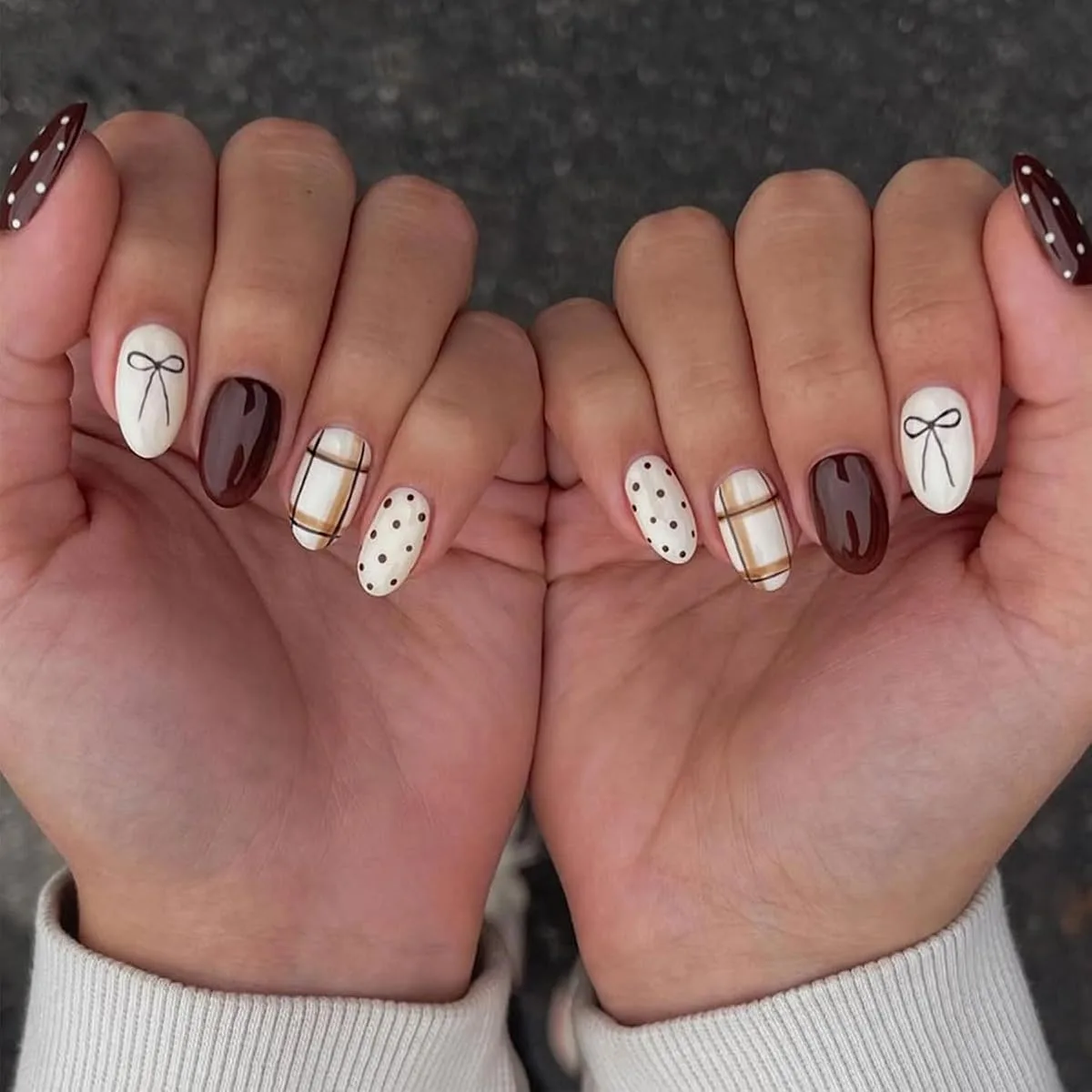 Both hands with short oval nails in deep brown, cream with black bow outline, cream and brown plaid, and brown polka dots