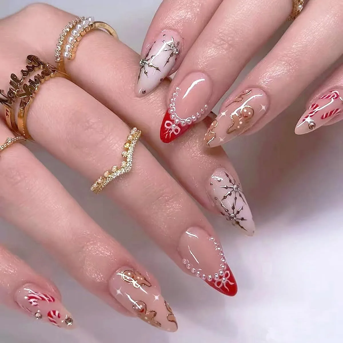 Long almond Christmas nails with silver starbursts, red French tips, gingerbread men and candy cane stripes