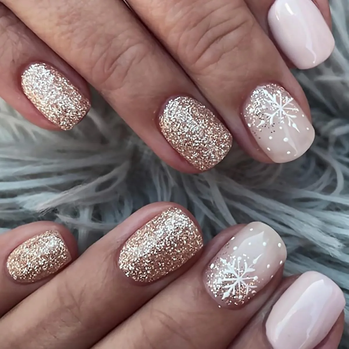 Champagne gold glitter and pale pink holiday nails with white snowflakes on short oval nails