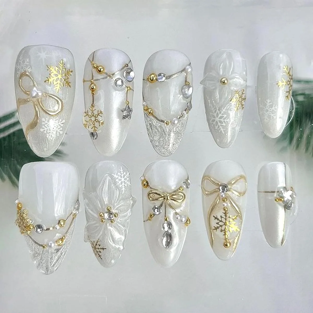 White winter fake nail ideas: press-on nail tips with gold snowflakes, gold bows, pearls, silver chains, 3D flowers and glitter