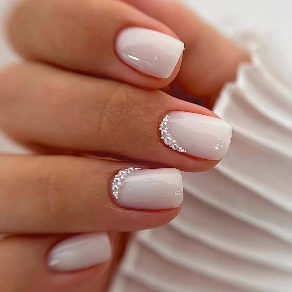 Short square nails in glossy milky white with pearl and rhinestone crescents at the cuticle