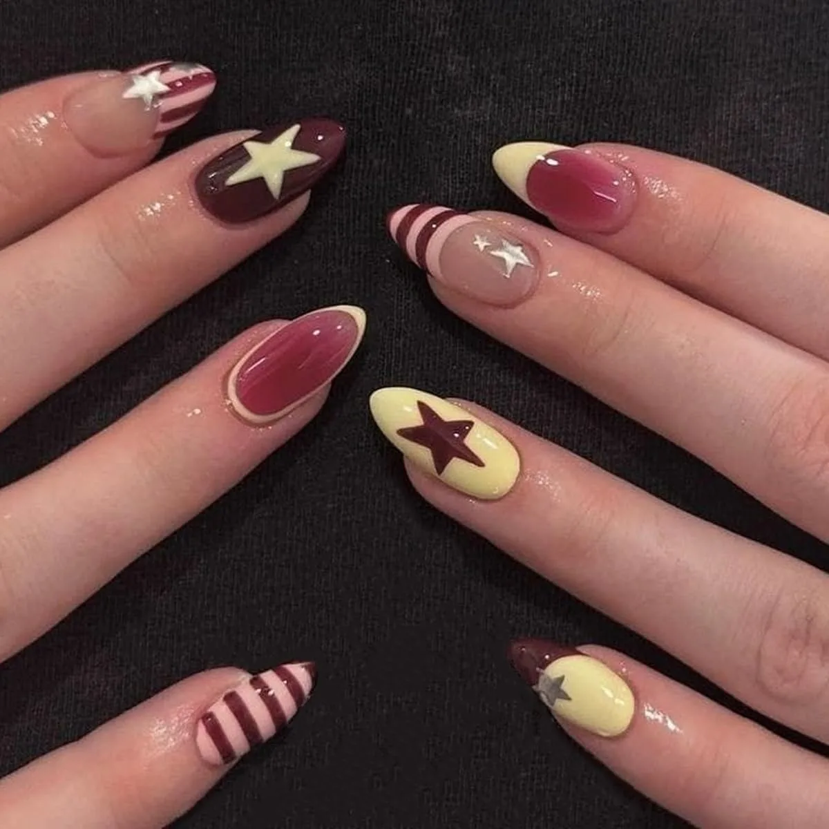 Short almond nails in burgundy and cream with stars, stripes and two tone French tips on a black background