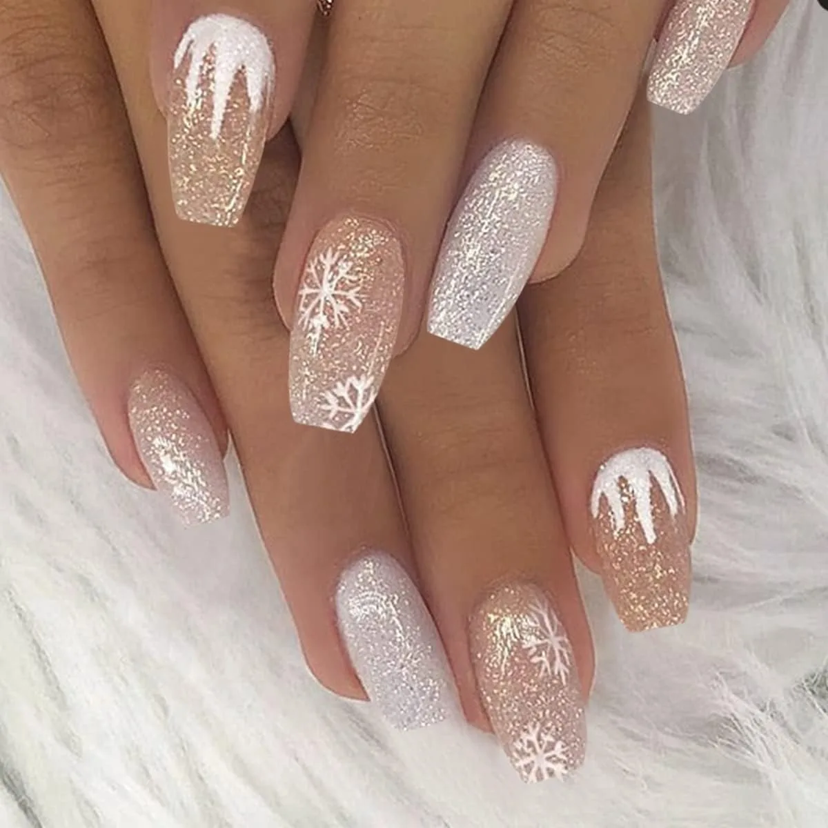 Long coffin nails in champagne and silver glitter with white snowflakes and white drip tips on a white furry background